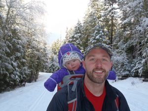 Shane J. with his daughter on a snowy trail in the woods.
