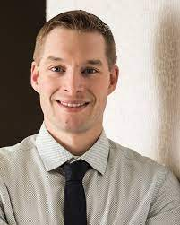 headshot of mike butler smiling at the camera in a shirt and tie